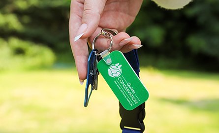 A hand holding a green key tag with the Quinte Conservation logo.